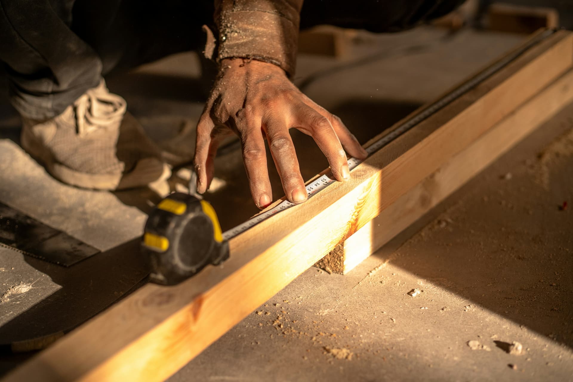 A carpenter's hand marking a measurement on framing timber in golden-hour light